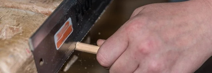 Hand sägt einen Holzdübel mit einer Feinsäge.